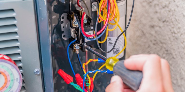 Close-up of HVAC technician working on wiring and electrical components of an air conditioning unit.