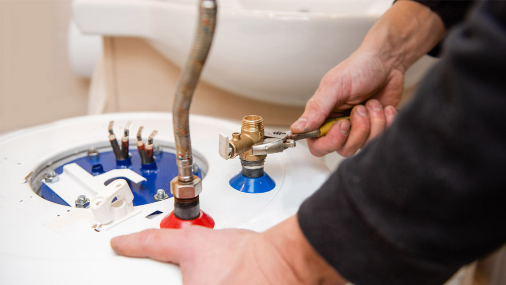 Plumber using pliers to repair a water heater valve.