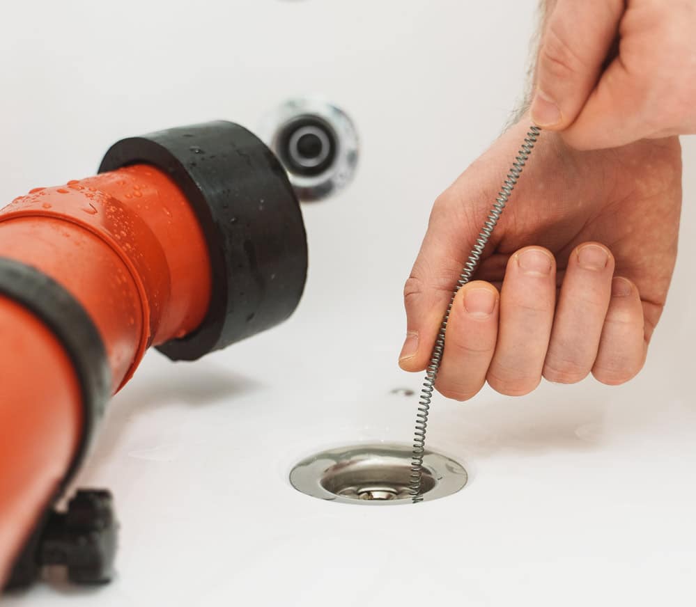 Close-up of a plumber using a drain snake to clear a clogged drain.