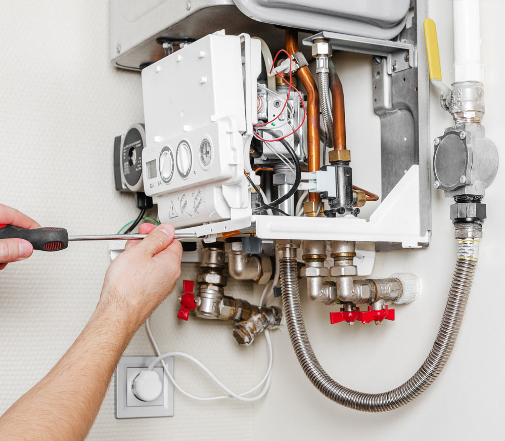 Technician repairing a gas boiler, using a screwdriver. Plumbing and control panel visible.