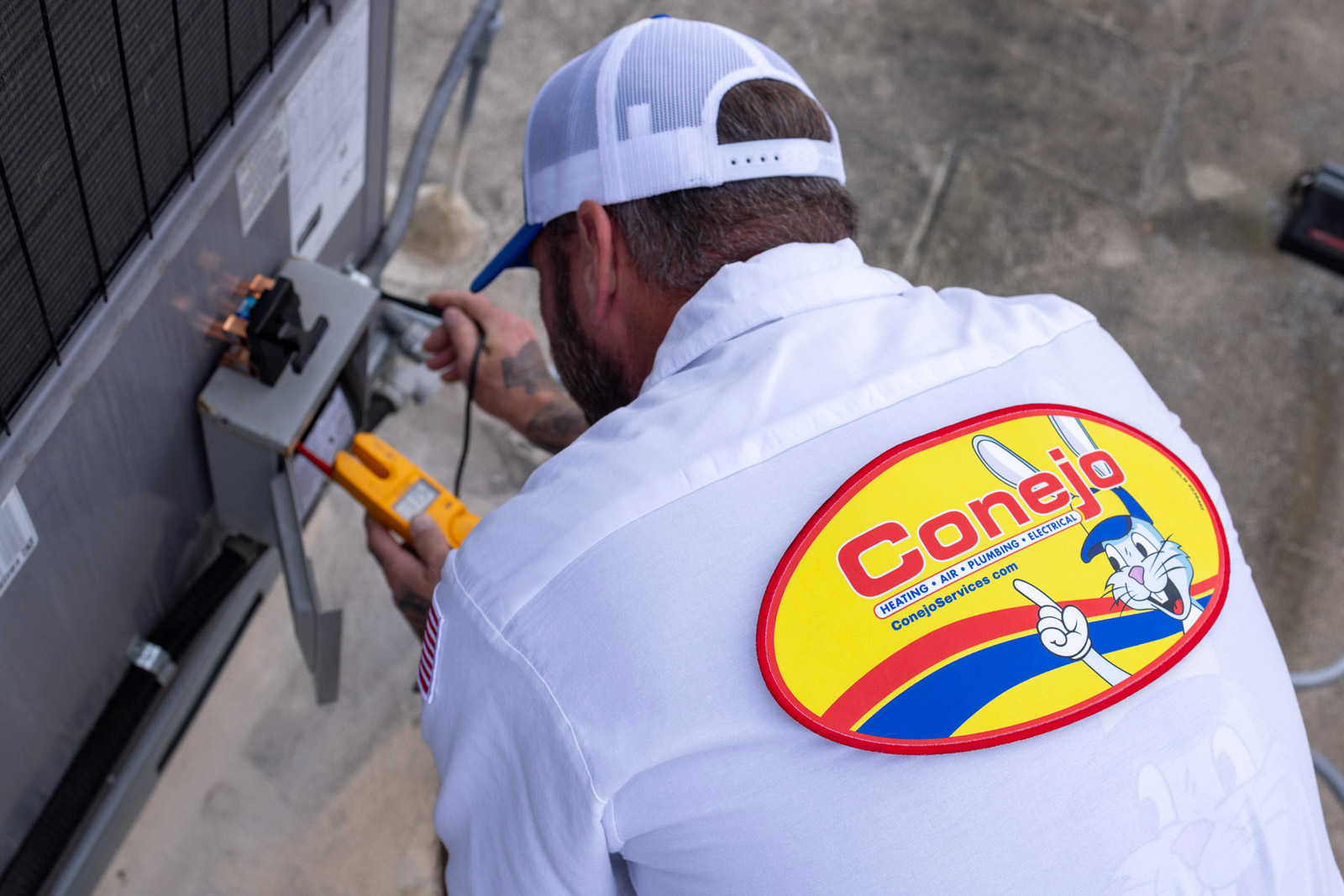 HVAC technician troubleshooting an air conditioning unit. Conejo Services logo on shirt.