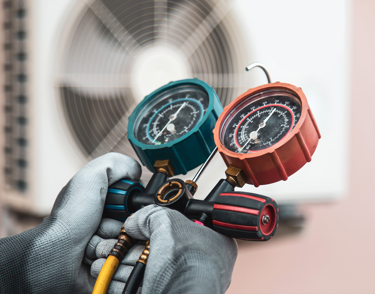 Technician's hands using gauges to check AC unit refrigerant pressure.