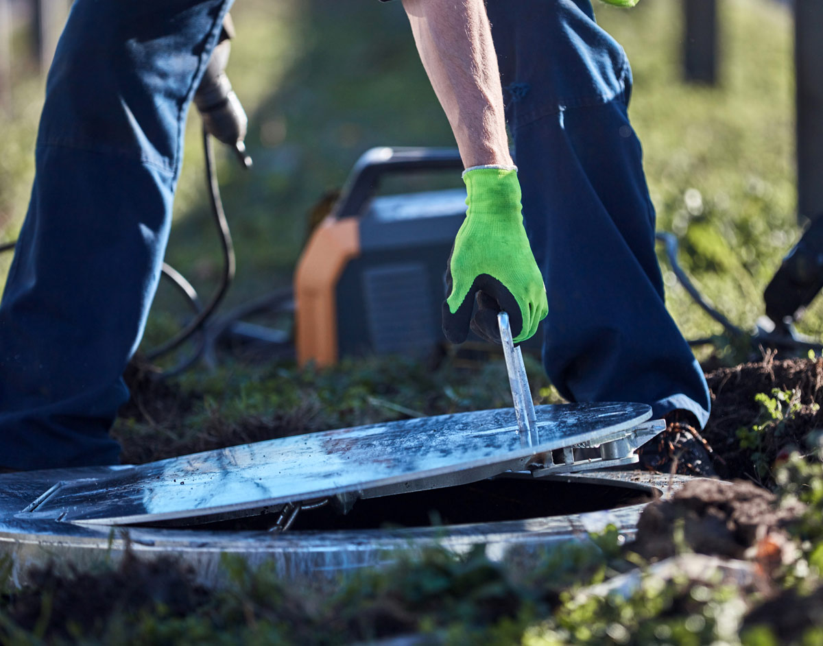 Worker using a tool to open a manhole cover.